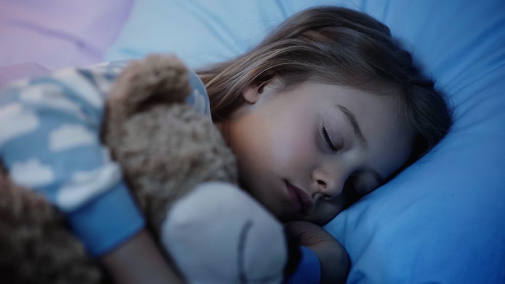 Preteen girl sleeping near blurred soft toy on bed at night. Child with ADHD peacefully sleeping in bed with toy