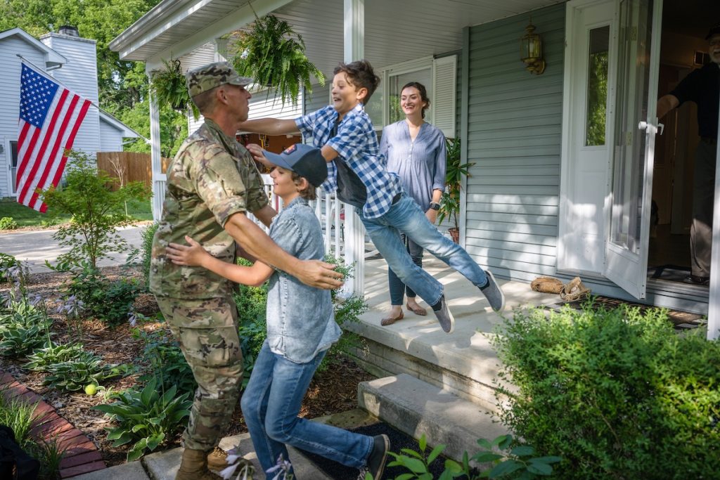 Air Force service member comes home to his family and  veteran father-in-law on the front porch.