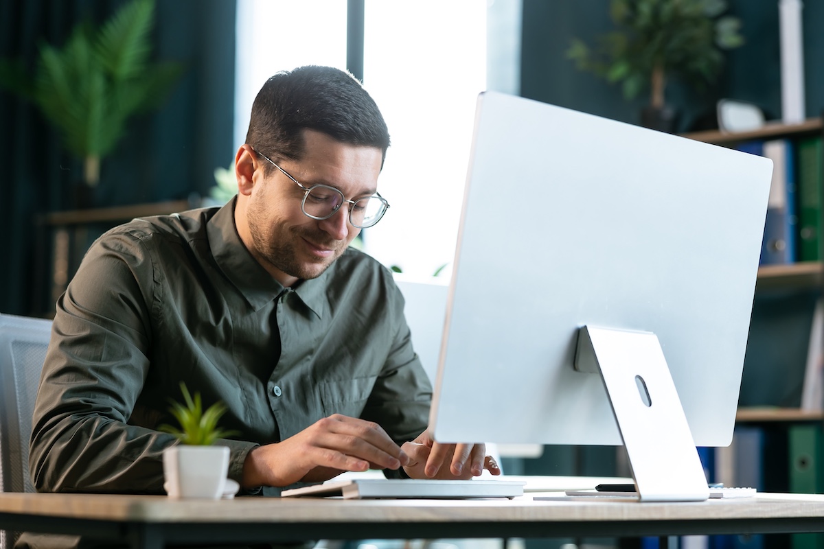 Focusing on work. Handsome young man looking on monitor and typing something while sitting on working place in creative office