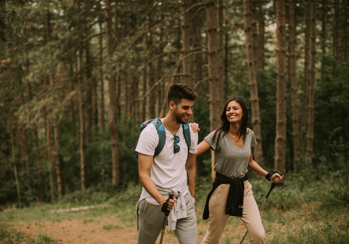 Couple of young hikers with backpacks walk through the forest