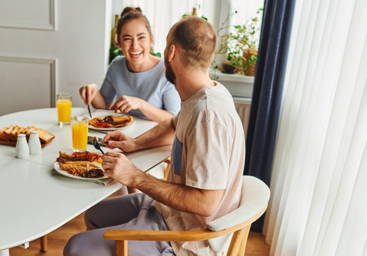Border collie sitting near laughing couple in homewear having breakfast in morning at home